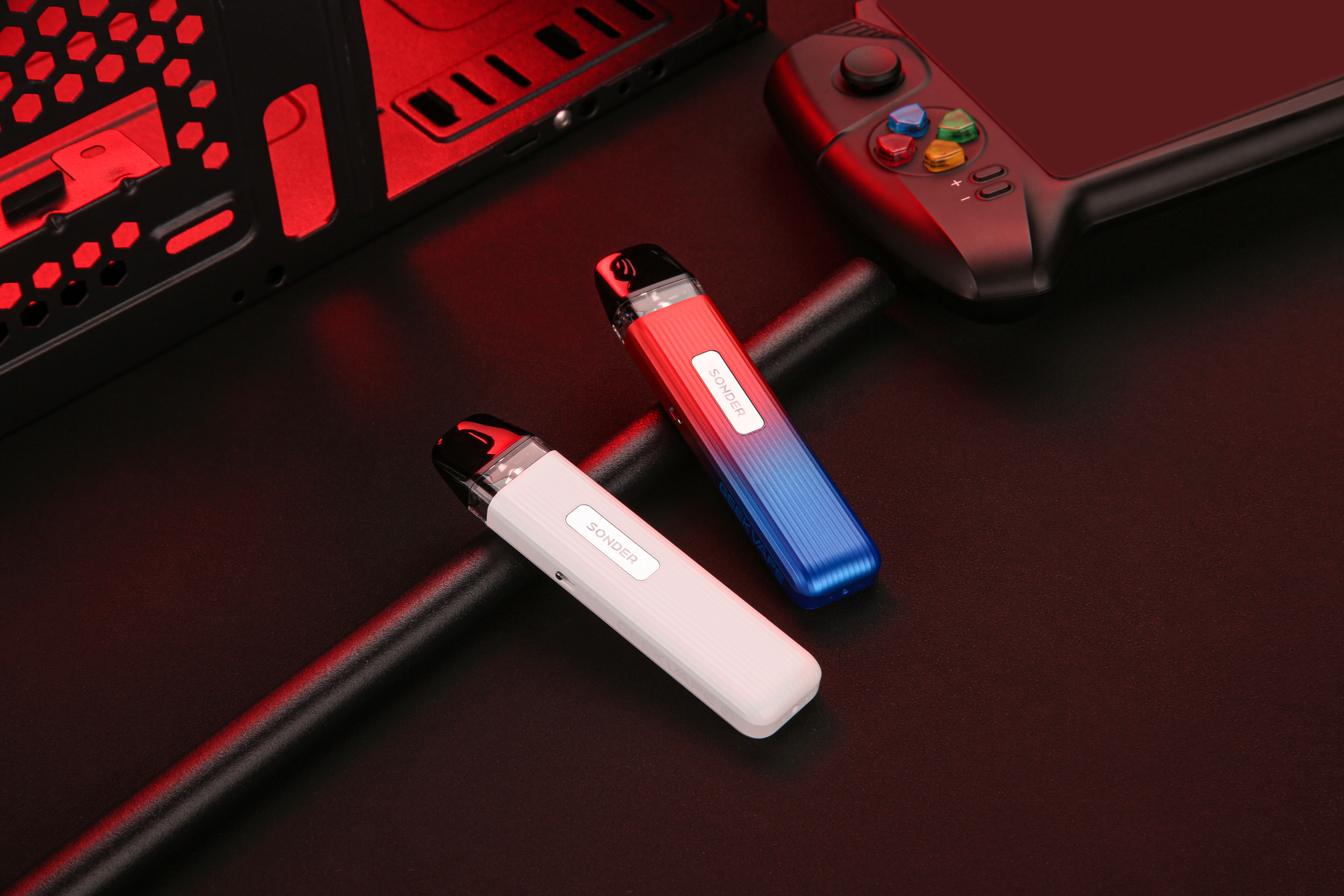 Sonder Q vape kits in red/blue and white placed next to a game console in a lifestyle scenario